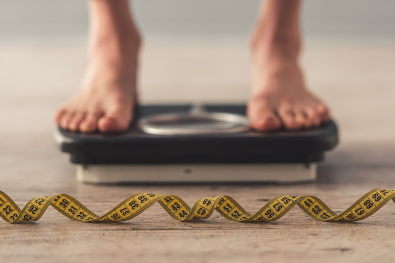 Cropped image of a person standing on weighing scales with grey background. (Shutterstock/VGstockstudio)